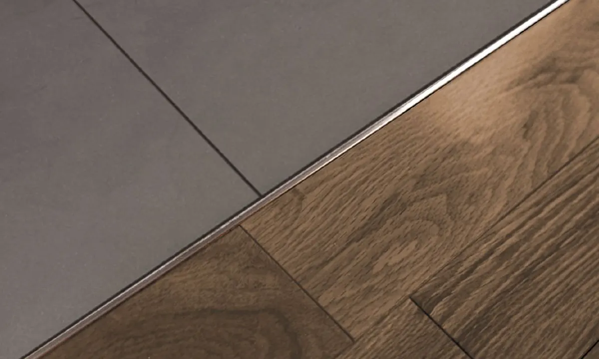 Thin metal Schluter profile where grey floor tile meets dark wood flooring
